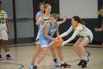 a child wearing a blue uniform dribbling a basketball, a child in a green and white uniform is trying to take it
