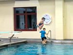 one scout is in mid-air jumping into the pool while another climbs out