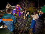 two people by a Christmas tree, people singing from song books