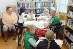 a man poses in a Christmas costume; children and an adult are around him crafting