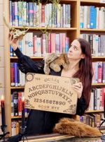 a woman holding an oija board holds up a deer skull